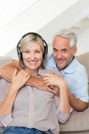 Smiling mature man embracing woman from behind on sofa at homeの写真素材