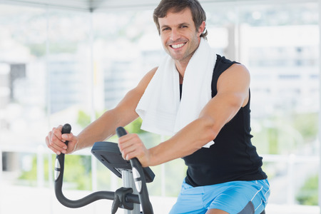Portrait of a smiling young man working out at spinning class in a bright gym