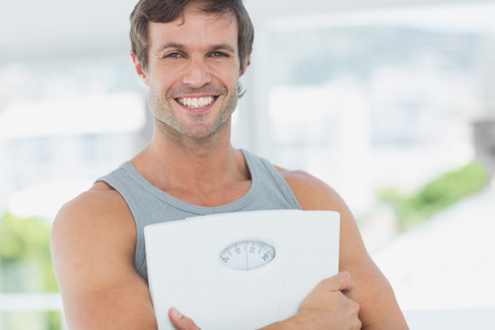 Portrait of a fit young man standing with scale in a bright exercise roomの写真素材