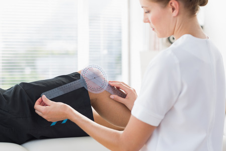 Female physiotherapist examining knee angle of man with goniometerの写真素材