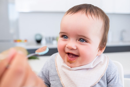 Cheerful baby boy being fed by mother at homeの写真素材