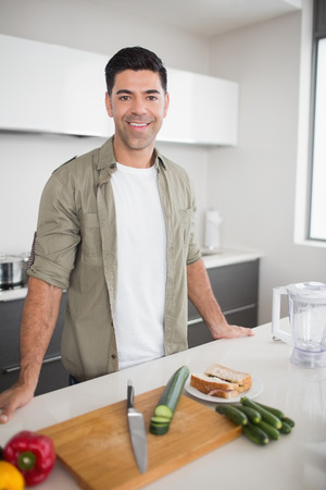 Portrait of a smiling man with vegetables and chopping board in the kitchen at homeの写真素材