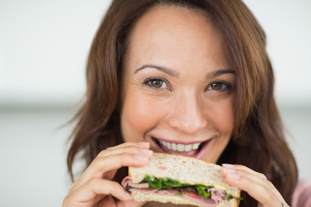 Closeup portrait of a beautiful smiling young woman eating sandwichの写真素材