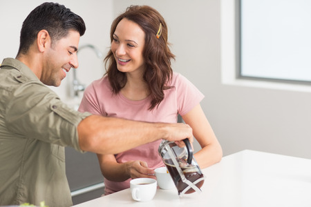 Happy young man pouring tea to womans cup in the kitchen at homeの写真素材