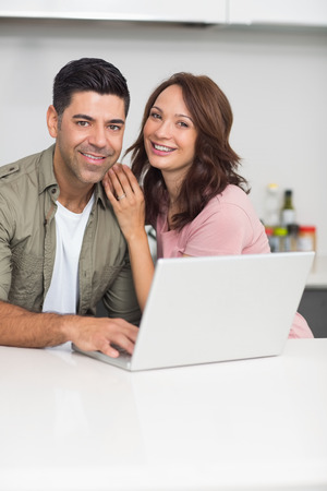 Portrait of a happy couple using laptop in the kitchen at homeの写真素材