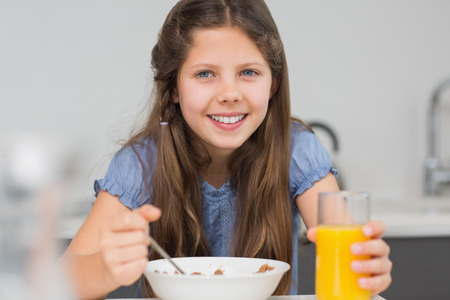 Portrait of a smiling young girl enjoying breakfast in the kitchen at homeの写真素材