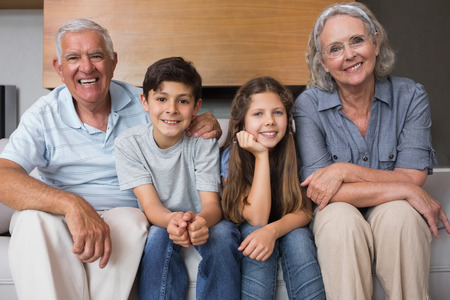 Portrait of grandparents and two kids sitting on sofa in the living room at homeの写真素材