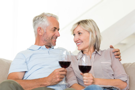 Portrait of a smiling mature couple with wine glasses sitting on sofa at homeの写真素材