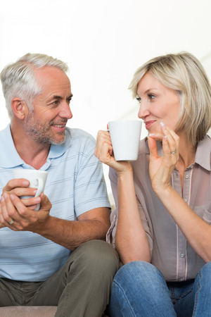 Portrait of a smiling mature couple with coffee cups sitting on sofa at homeの写真素材
