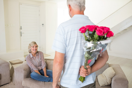 Rear view of a man holding bouquet behind his back with woman sitting on couch at homeの写真素材