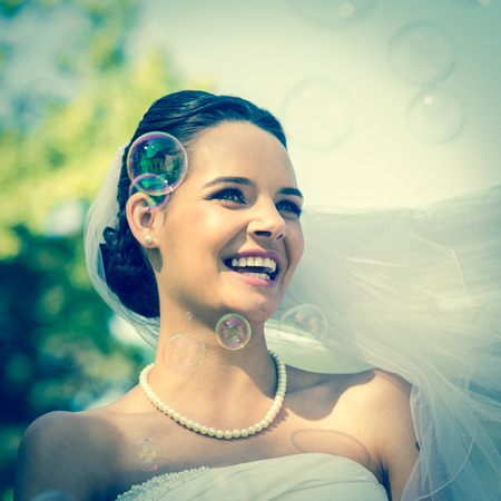 Close-up of a young beautiful bride looking at soap bubbles in the parkの写真素材
