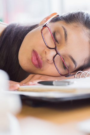 Closeup of beautiful young businesswoman sleeping on desk in officeの写真素材
