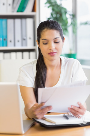 Beautiful young businesswoman reading documents at office deskの写真素材