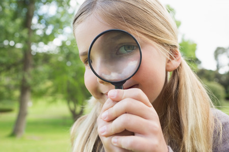 Close-up portrait of a cute young girl looking through magnifying glass at the parkの写真素材