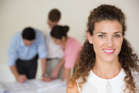 Portrait of beautiful businesswoman with collaegues working in background at officeの写真素材