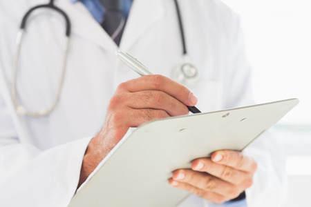 Midsection of male doctor writing on clipboard in hospitalの写真素材