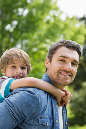 Side view portrait of a father carrying young boy on back at the parkの写真素材