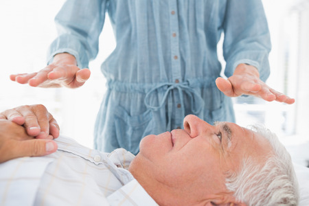 Senior man receiving Reiki treatment by massage therapist at spaの写真素材