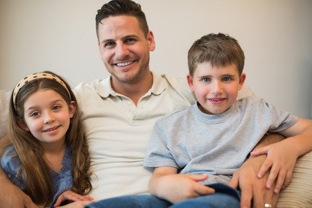 Portrait of father and children smiling while sitting on sofaの写真素材