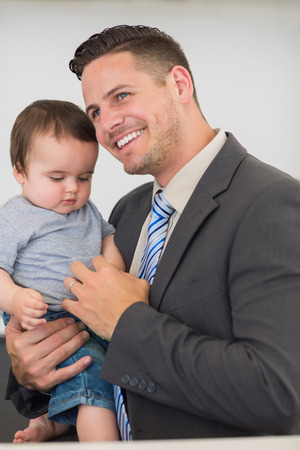 Happy businessman carrying baby boy while looking away at homeの写真素材
