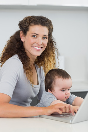 Portrait of beautiful woman with baby boy using laptop at counterの写真素材