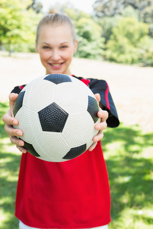 Portrait of female soccer player showing ball at parkの写真素材