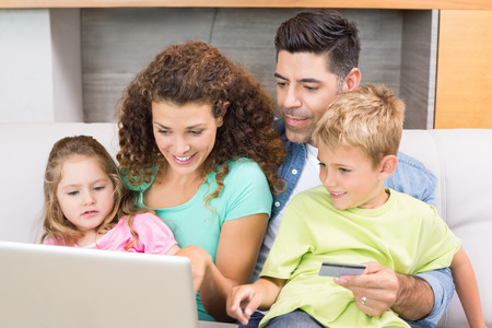 Cheerful family sitting on sofa with laptop shopping online at home in living roomの写真素材