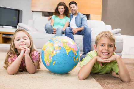 Smiling siblings lying on the rug with a globe at home in living roomの写真素材