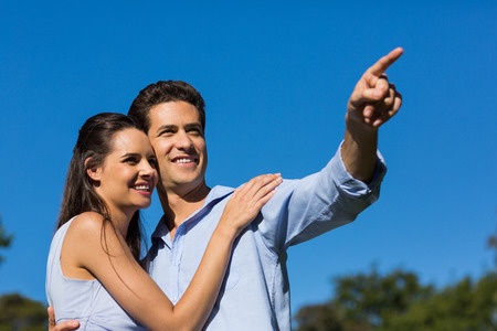 Loving and happy young couple looking away against clear blue skyの写真素材