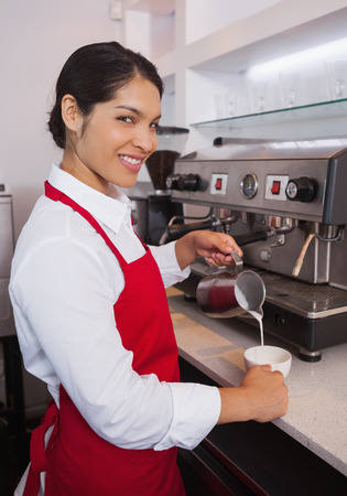 Pretty barista pouring milk into cup of coffee in a cafeの写真素材