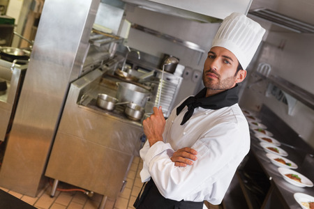 Focused chef looking at camera with arms crossed holding ladle in a commercial kitchen