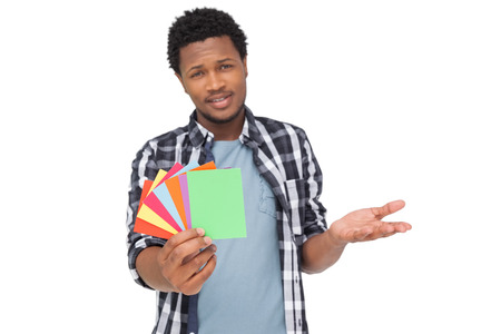 Portrait of a confused young man holding colorful papers over white backgroundの写真素材