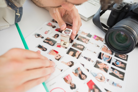 Concentrate male artist sitting at desk with photos in the officeの写真素材