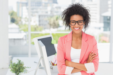 Portrait of a casual female artist standing with arms crossed at a bright officeの写真素材