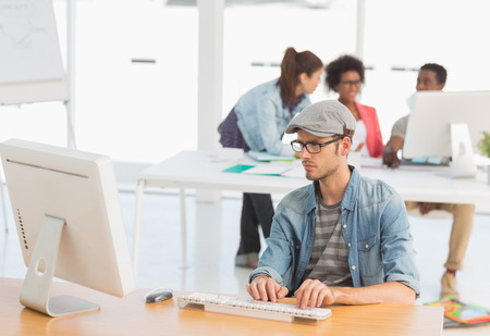 Casual male artist using computer with colleagues in the background at a bright officeの写真素材