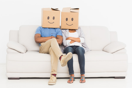 Young couple with happy smiley boxes over faces while sitting on sofaの写真素材