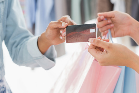 Closeup mid section of female customer receiving shopping bags and credit card from saleswoman in boutiqueの写真素材
