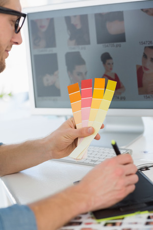 Handsome designer working with digitizer holding colour chart at his desk in creative officeの写真素材