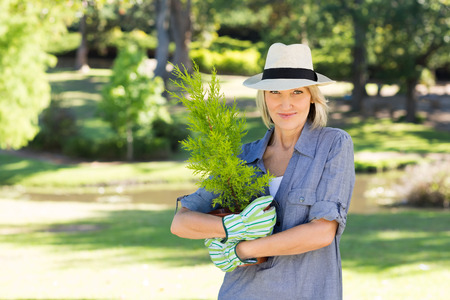 Portrait of happy woman holding pot plant in gardenの写真素材