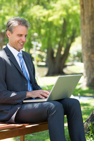 Smiling businessman using laptop at parkの写真素材