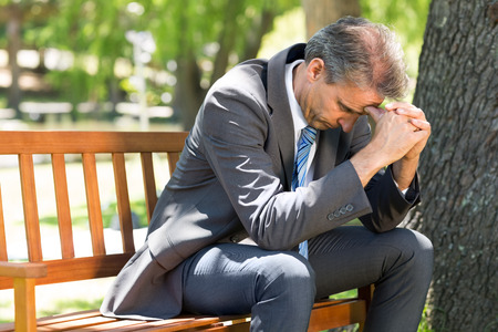 Upset mature businessman sitting on park benchの写真素材