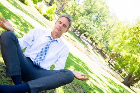 Mature businessman doing yoga on grass in parkの写真素材