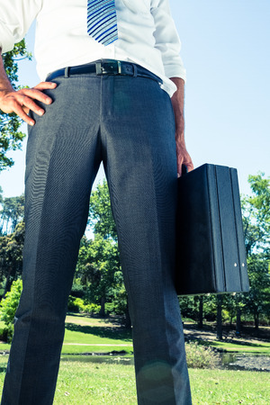 Midsection of businessman with hand on hip carrying briefcase at parkの写真素材