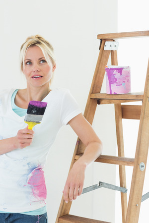 Beautiful young woman with paint brush looking away in the new houseの写真素材