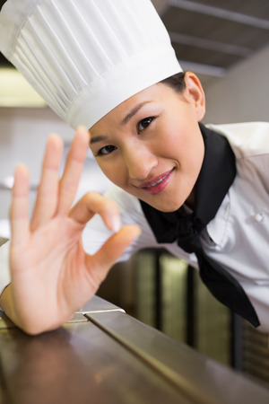 Closeup portrait of a smiling female cook gesturing okay sign in the kitchenの写真素材
