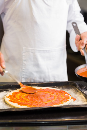 Closeup mid section of a male chef preparing pizza in kitchenの写真素材