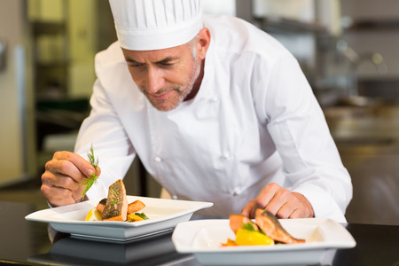 Closeup of a concentrated male chef garnishing food in the kitchenの写真素材