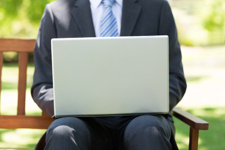 Midsection of businessman using laptop while sitting on park benchの写真素材
