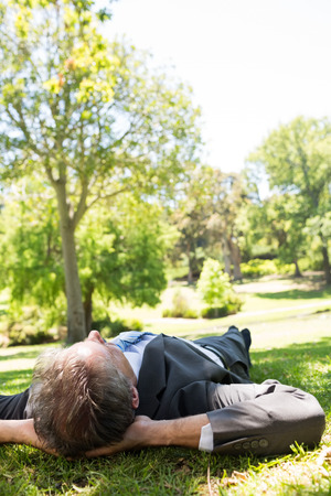 Relaxed businessman lying on grass in parkの写真素材