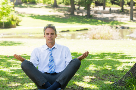 Relaxed mature businessman meditating on grass in parkの写真素材